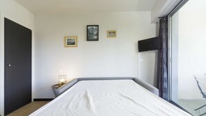 Quarto com cama, mesa de cabeceira, televisão e janela.