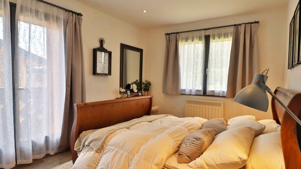 A bedroom with a bed, a bedside lamp, a dresser, and a window with curtains.