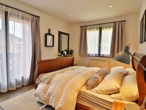 Un dormitorio con cama, lámpara de noche, cómoda y ventana con cortinas.