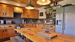 A modern kitchen with wooden cabinets, a large island, a built-in oven, and a stainless steel refrigerator.