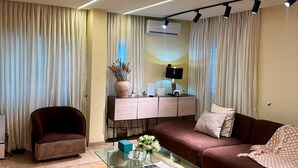 Ein modernes Wohnzimmer mit Glastisch, Sofa, Sessel, Schreibtisch mit Computer und Fernseher.