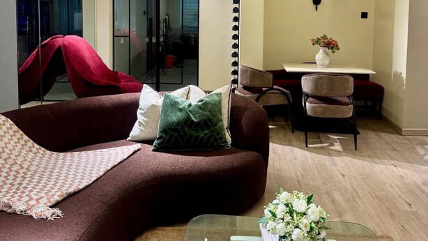Ein modernes Wohnzimmer mit einem braunen Sofa, einem Glastisch und einem Essbereich mit einem weißen Tisch und Stühlen.