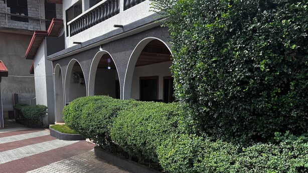 Ein Gebäude mit rotem Dach, einem Balkon mit schwarzen Geländern und einer Hecke entlang des Weges.