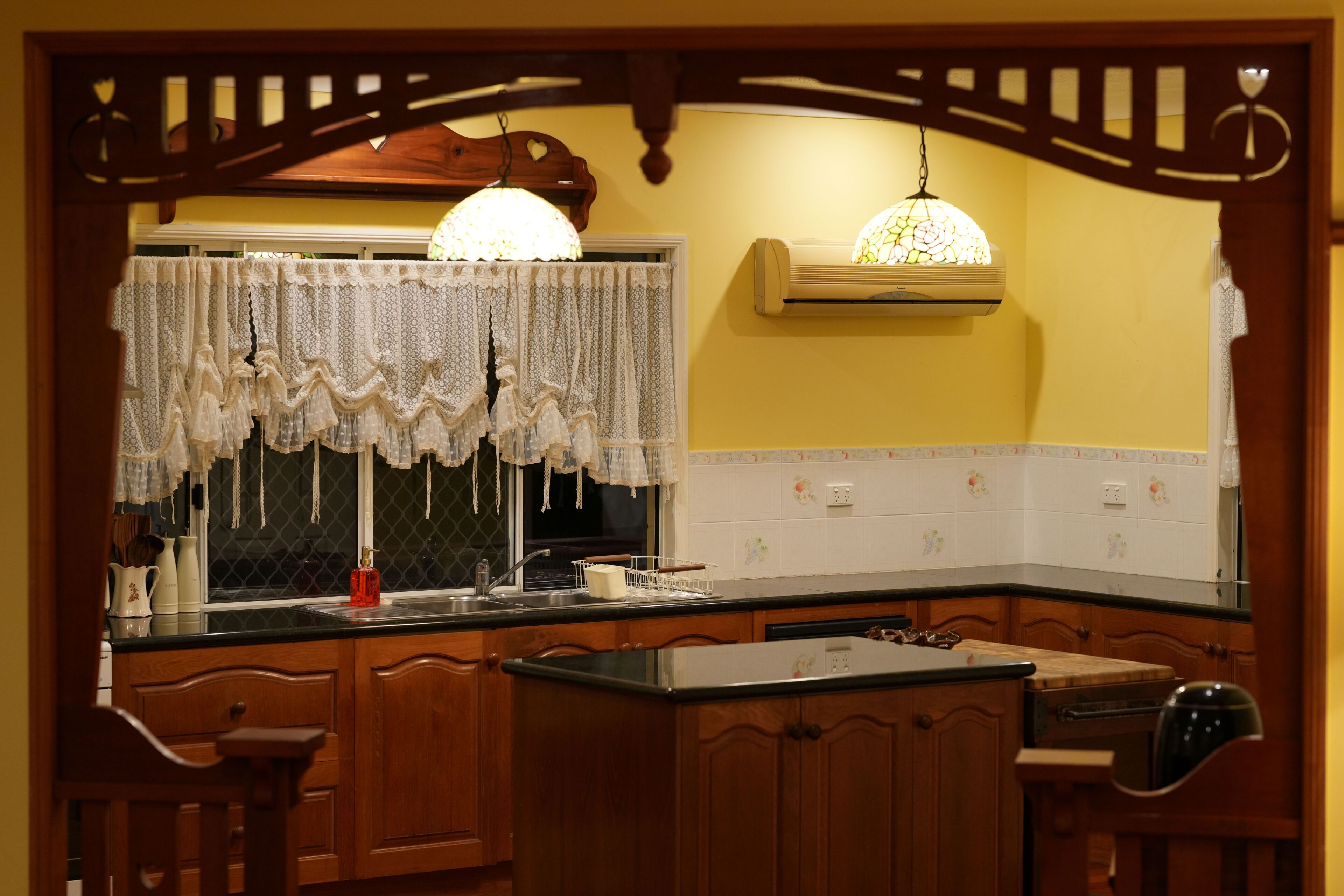 A kitchen with wooden cabinets, a black countertop, a sink, and a hanging light fixture.