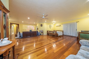 A spacious living room with hardwood flooring, a ceiling fan, a piano, and a dining table.