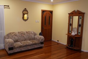 Una habitación con piso de madera, un sofá floral, una puerta de madera, un espejo y un mueble con puerta de vidrio.