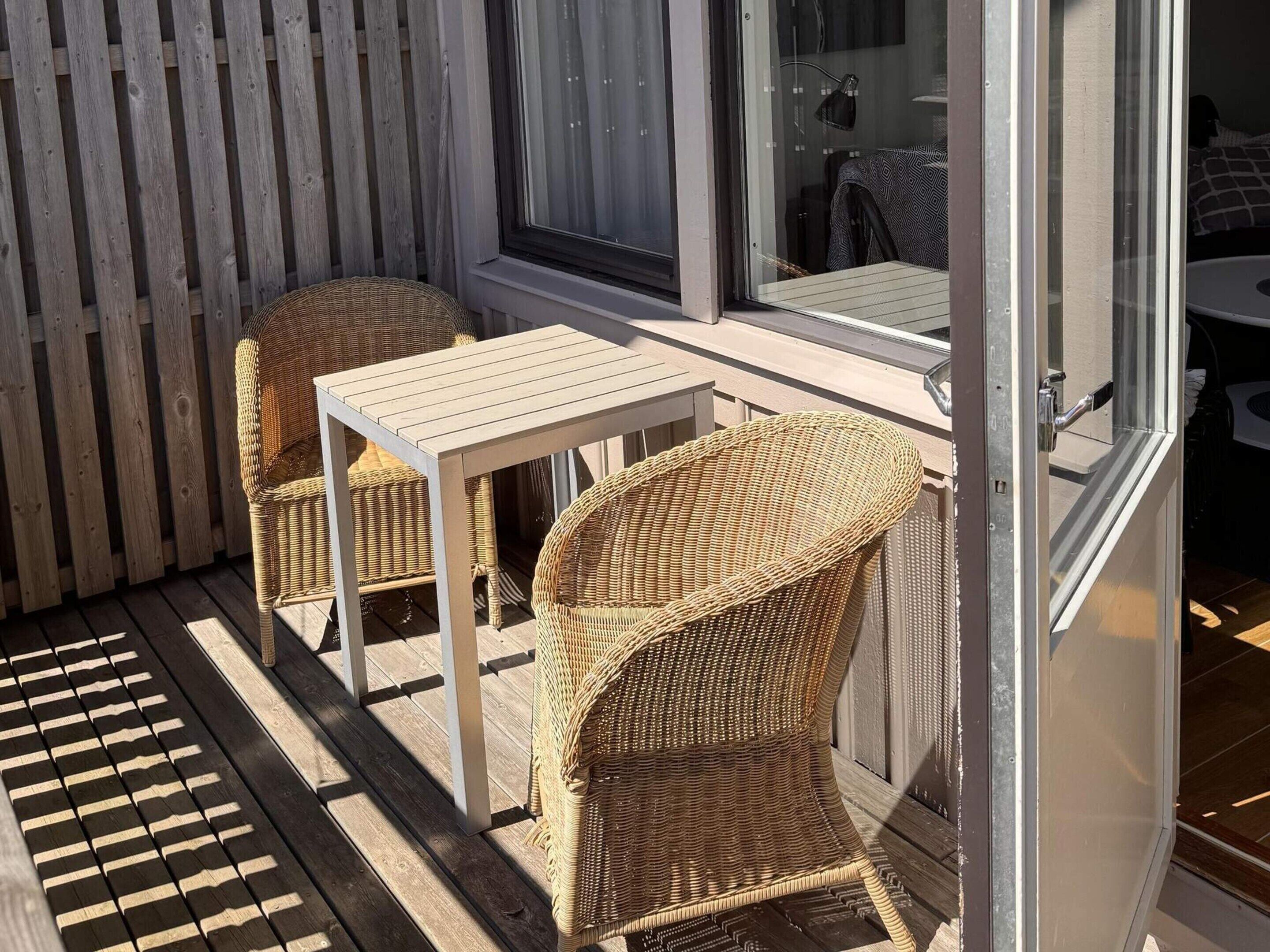 A patio with wicker furniture and a table, a wooden fence, and a window.