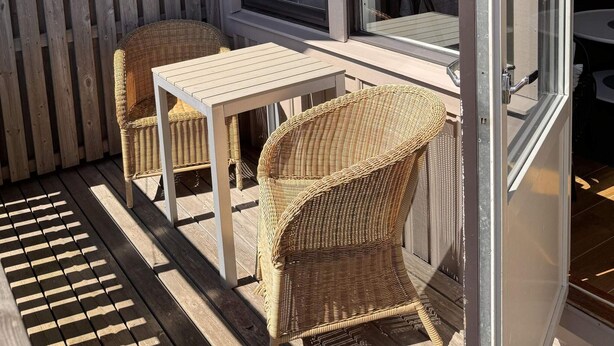 Un patio con muebles de mimbre, una mesa, una valla de madera y una ventana.