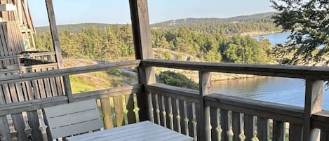 Terraza de madera con una mesa y sillas, con vista a un lago y un bosque.