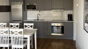 A compact kitchen with grey cabinets, a built-in oven, a coffee maker, and a dining area with white chairs. - 4 Star Holiday Home in Uddevalla (Uddevalla)