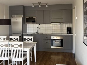 A compact kitchen with grey cabinets, a built-in oven, a coffee maker, and a dining area with white chairs. - 4 Star Holiday Home in Uddevalla (Uddevalla)