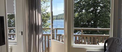 A room with a view of a lake, a chair, and a window with a view of a deck.