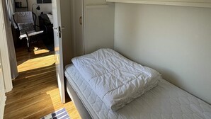 Un dormitorio con una cama individual, una silla, una estantería con libros y una puerta que da a otra habitación.