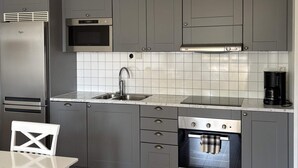 Una cocina moderna con armarios grises, un refrigerador de acero inoxidable, un microondas, una cafetera y un horno empotrado.
