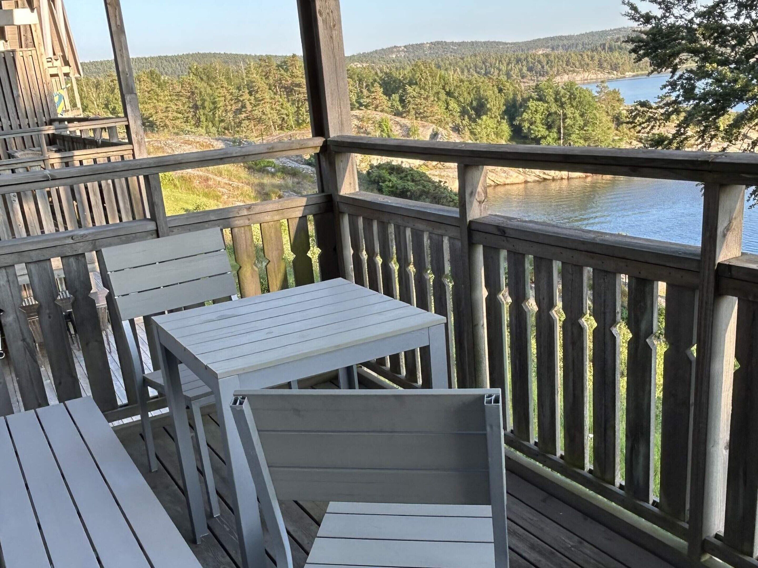 A wooden deck with a table and chairs, overlooking a lake and forested hills.