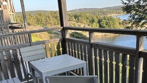 A wooden deck with a table and chairs, overlooking a lake and forested hills. - 4 Star Holiday Home in Uddevalla (Uddevalla)