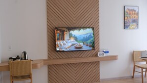 Una habitación moderna con una televisión de pantalla plana montada en una pared de madera, una silla de mimbre, una computadora portátil sobre una mesita y un cuadro enmarco.