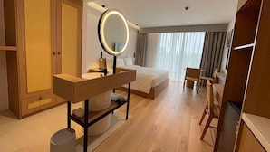 Una habitación de hotel con cama, mesita de noche, espejo, armario de madera y una zona de estar con sillones.