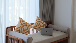 Una cama con una computadora portátil, dos almohadas estampadas y cortinas de gasa.