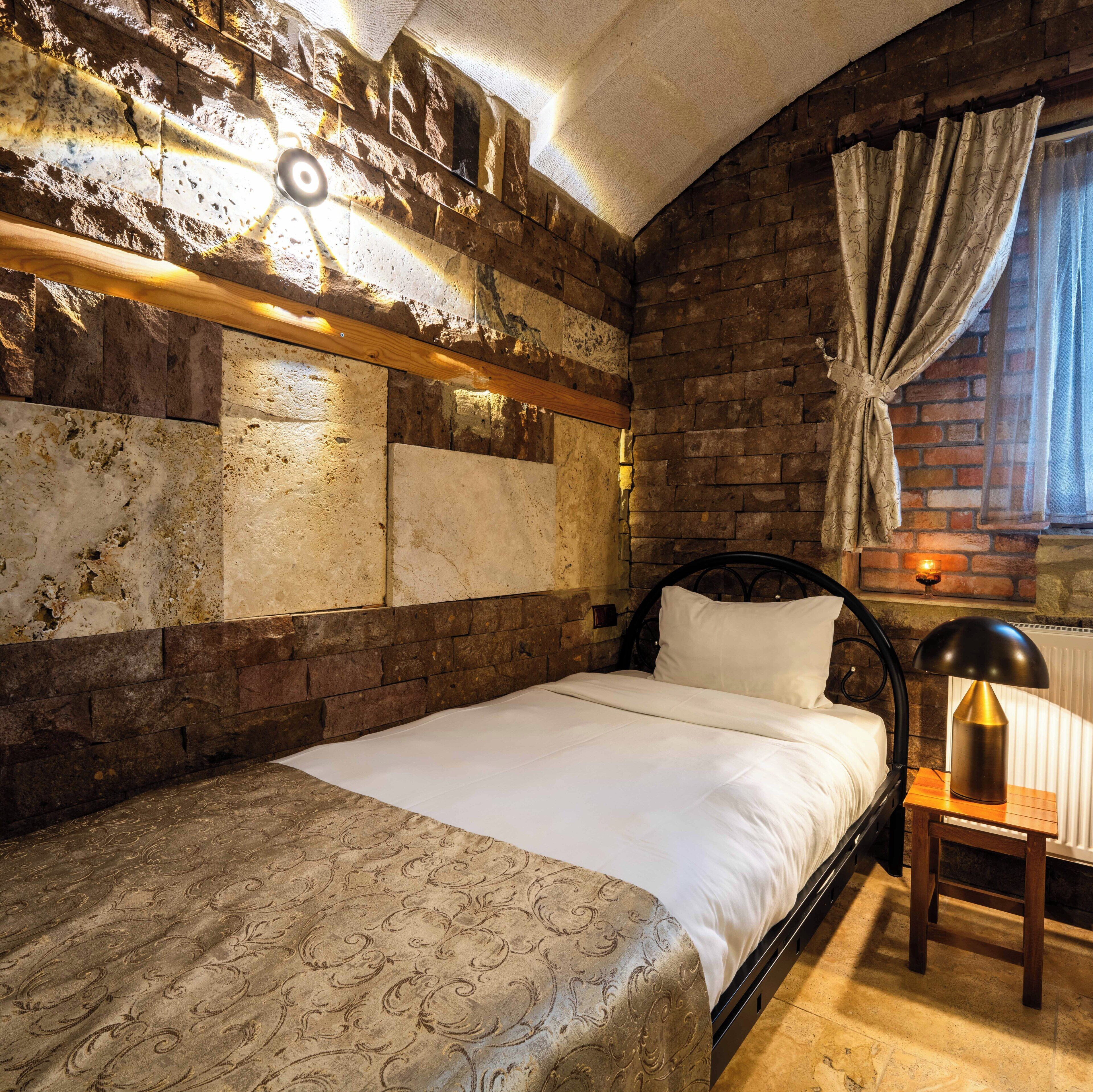Una cama en una habitación con paredes de piedra, un cabecero de madera y una mesita de noche con una lámpara.
