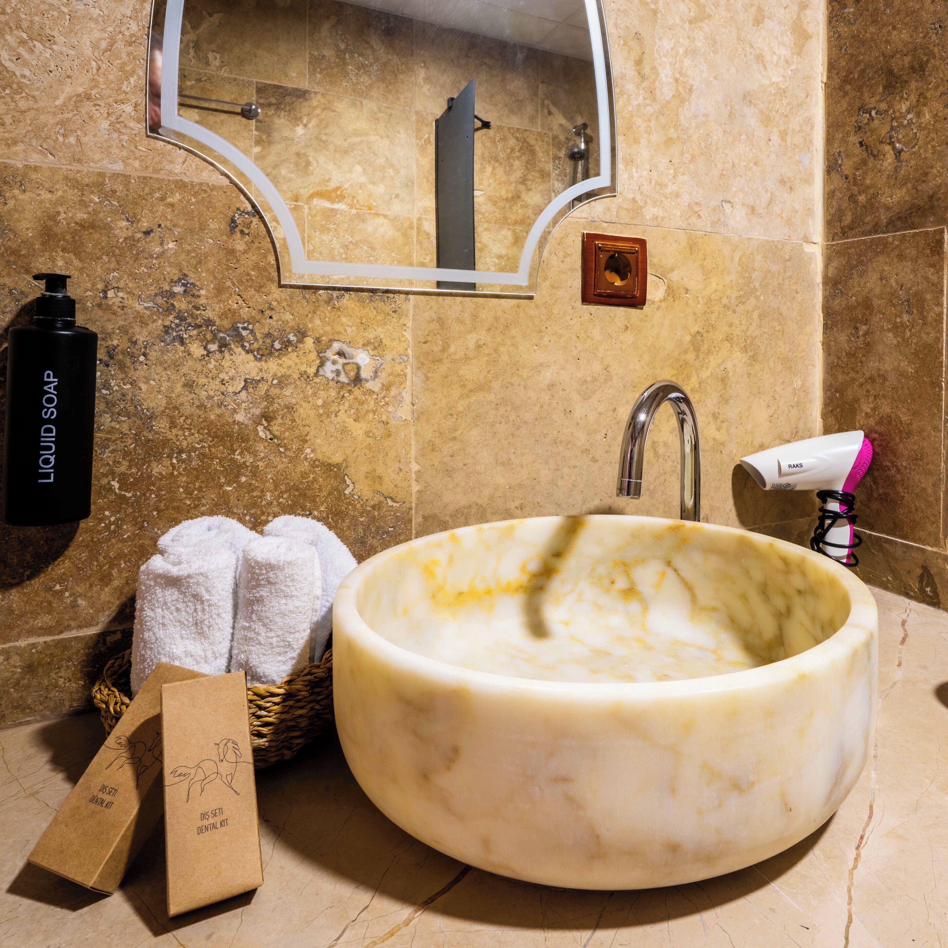 Un baño con lavamanos de mármol, espejo, toallero, dispensador de jabón y secador de pelo.