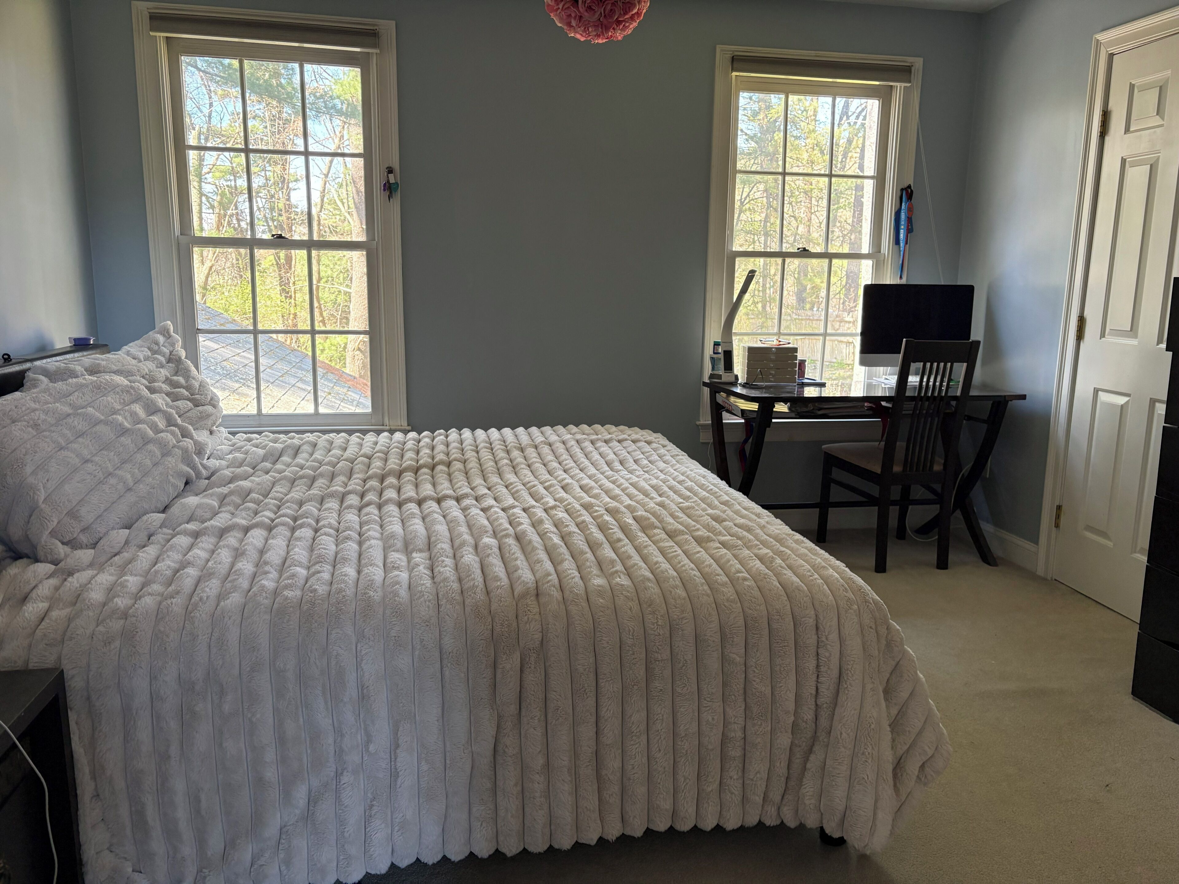 A bedroom with a large bed, two windows, a desk with a chair, and a TV.
