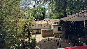 Un patio con mesa y sillas, una zona cubierta y un edificio con tejado de baldosas.
