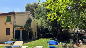 Un patio con mobiliario exterior, un edificio de fachada amarilla y abundante vegetación circundante.