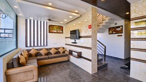 Un hall con sofá, televisor, escalera y mostrador de recepción.
