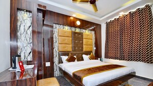 Habitación de hotel con pared de mármol, cama con cabecera de madera, escritorio, una silla y cortina estampada.