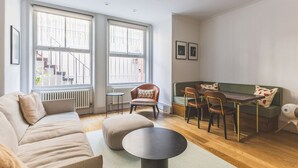 A living room with a sofa, ottoman, round coffee table, dining table with chairs, and a radiator. - Notting Hill Patio Retreat (London)