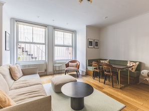 A living room with a sofa, ottoman, round coffee table, dining table with chairs, and a radiator. - Notting Hill Patio Retreat (London)