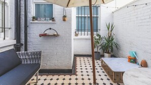 A courtyard with a tiled floor, a bench, a table, an umbrella, and potted plants. - Notting Hill Patio Retreat (London)