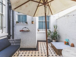 A courtyard with a tiled floor, a bench, a table, an umbrella, and potted plants. - Notting Hill Patio Retreat (London)