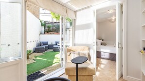 Una habitación con una cama, una mesita pequeña y vistas a un jardín a través de una puerta abierta.