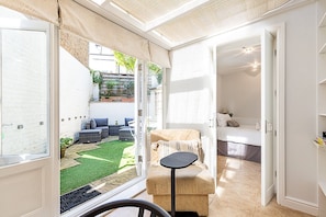 Ein Zimmer mit einem Bett, einem kleinen Tisch und Blick auf einen Garten durch eine offene Tür.