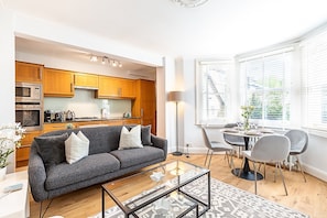Ein modernes Wohnzimmer mit einem grauen Sofa, einem Glastisch und einem Essbereich mit Tisch und Stühlen.