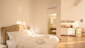 A bedroom with a bed, a nightstand, a bathroom visible through an open door, and a kitchenette area.
