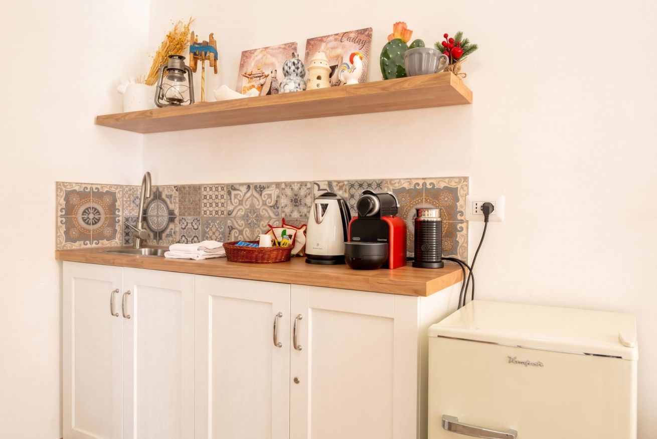 Cocina con armarios blancos, encimera de madera, refrigerador antiguo y objetos decorativos en un estante.
