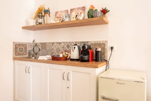 Una cucina con mobili bianchi, un piano di lavoro in legno, un frigorifero vintage e oggetti decorativi su uno scaffale.