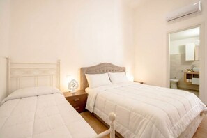 A bedroom with two beds, a nightstand, a bedside table, and a wall-mounted air conditioner. - Vecchia Bari Castello Svevo | Historic Charm with Balcony  (Bari)