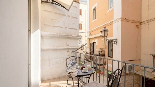 A narrow outdoor balcony with a table set for two, a chair, and a small table lamp.