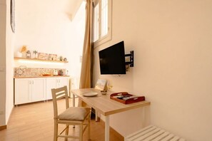Una cucina compatta con mobili bianchi, un tavolo di legno e una TV montata a parete.