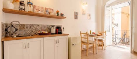 A kitchen with white cabinets, a countertop, and a refrigerator. There is a dining area with a table and chairs.