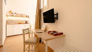 A compact kitchen with white cabinets, a wooden table, and a TV mounted on the wall.