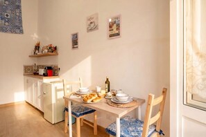 A dining area with a table set for two, a refrigerator, and a shelf with kitchen items. - Vecchia Bari Castello Svevo | Historic Charm with Balcony  (Bari)