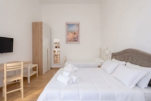 Una camera d'albergo con un letto, una scrivania, un armadio, una televisione e un quadro appeso al muro.