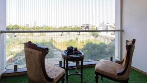 Ein Balkon mit zwei Holzstühlen, einem kleinen runden Tisch mit Tablett und Blick auf die Stadt durch ein Metallgeländer.