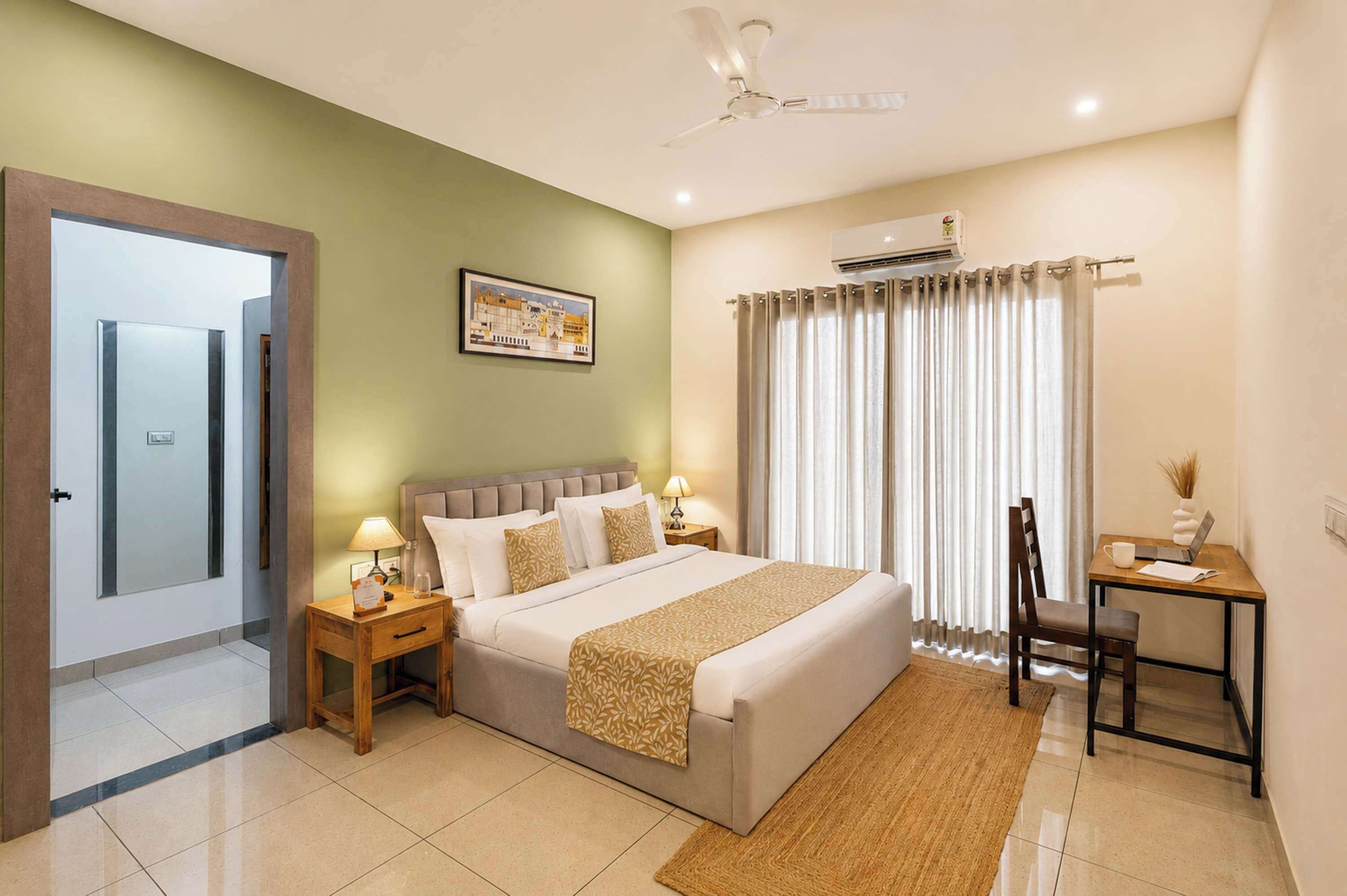 Habitación de hotel con cama, mesitas de noche, escritorio, silla, ventilador de techo y aire acondicionado.