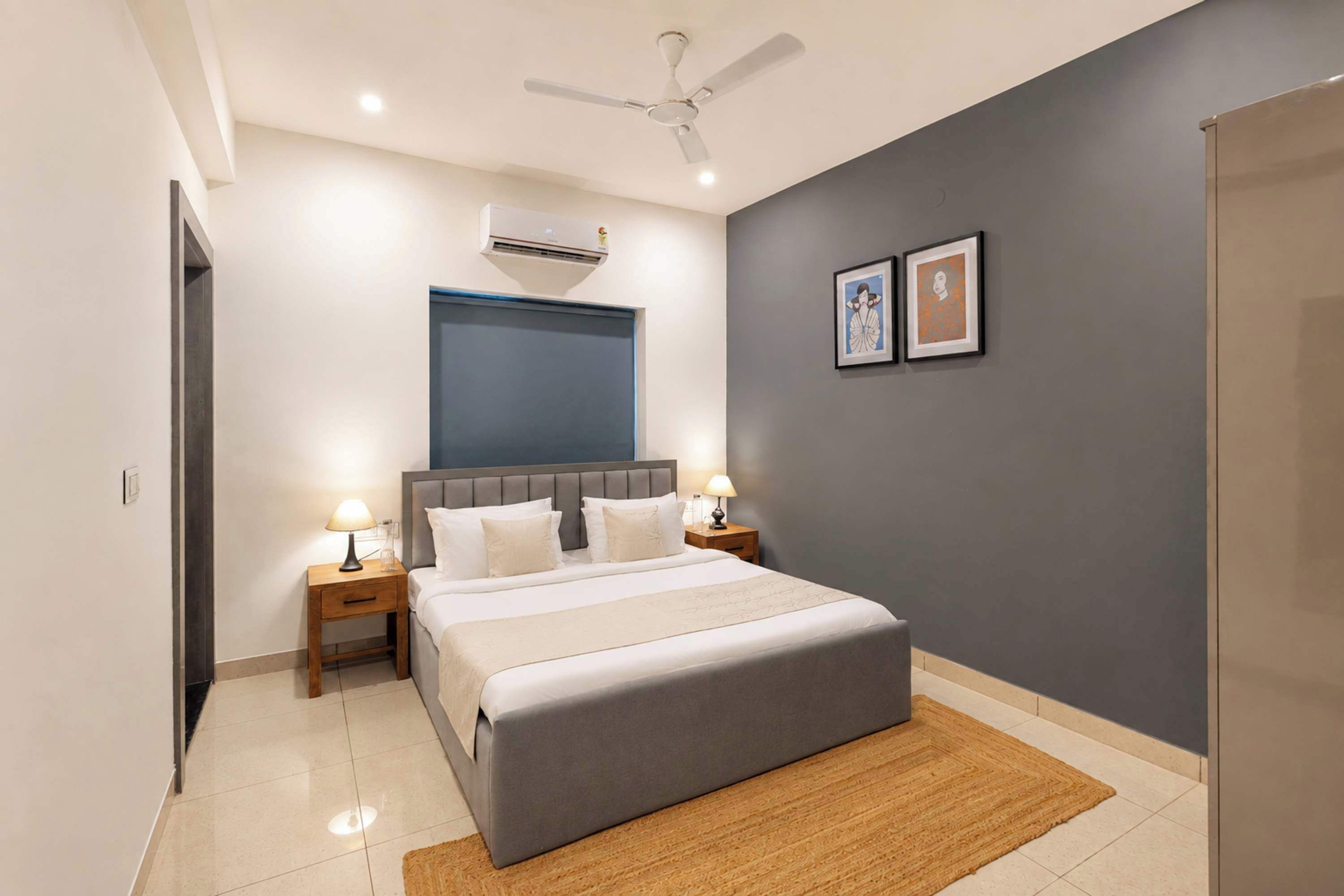 A bedroom with a bed, nightstands, a ceiling fan, an air conditioner, and two framed pictures on the wall.